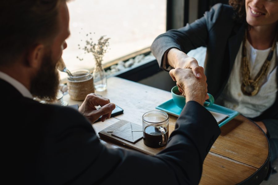 man and woman shaking hands over table with coffee